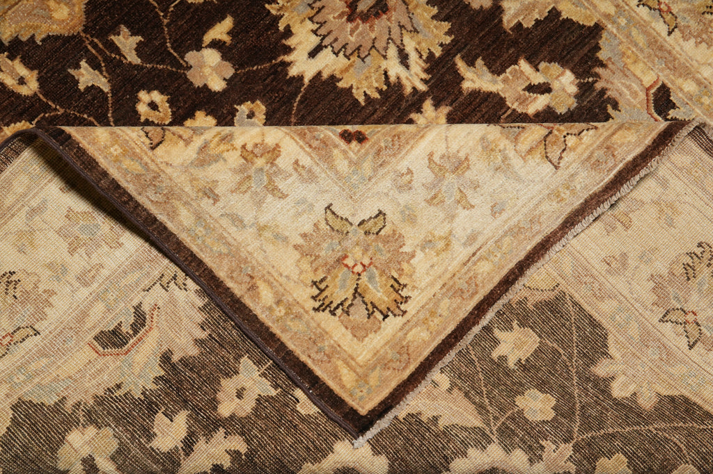 A close-up of a traditional oriental-style rug with a folded corner revealing its cream and brown patterned underside, set against a matching dark brown floral rug.