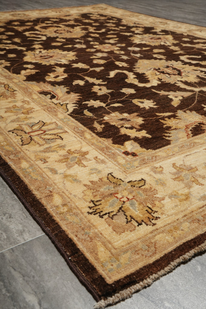 A traditional oriental area rug with a dark brown floral pattern on a beige background, shown laid out on a gray tiled floor.