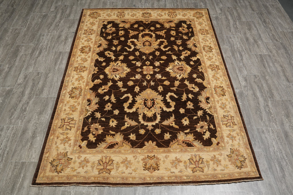 A rectangular area rug with an ornate floral and medallion pattern, featuring a dark brown center and a beige border, laid out on a gray wood-look floor.
