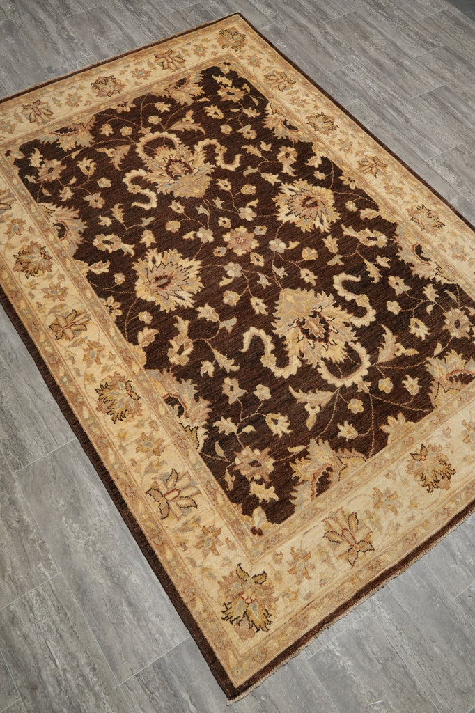 A rectangular area rug with a traditional floral pattern, featuring a dark brown center and a beige border, laid out on a gray wood-look floor.
