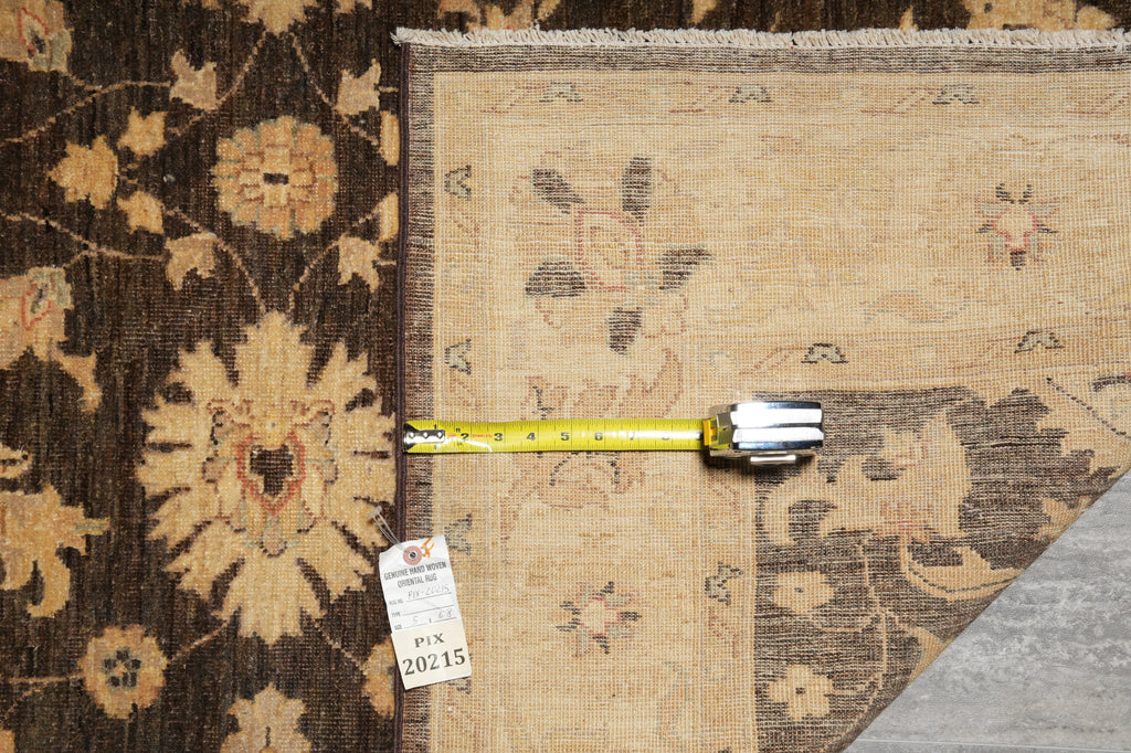 A close-up of two patterned rugs laid side by side, with a yellow tape measure placed horizontally across the edge and a white tag hanging from the tape. One rug is dark brown with large floral motifs, and the other is a lighter beige with subtle floral and geometric patterning.