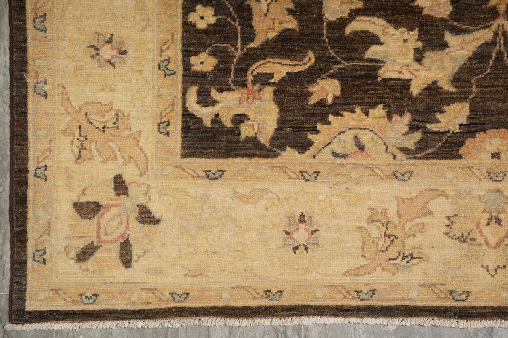 Close-up of an ornate traditional rug corner showing a cream and dark brown floral pattern with a decorative border and small fringe.