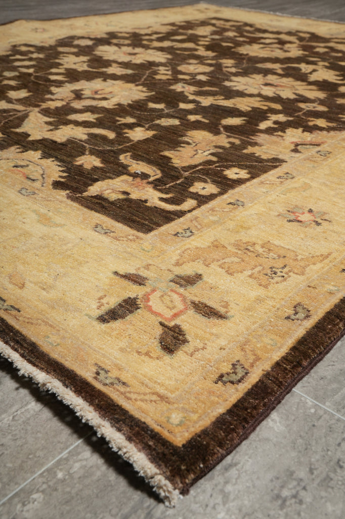 A traditional oriental-style area rug with a dark brown floral field and a beige border, shown laid out on a gray tiled floor.