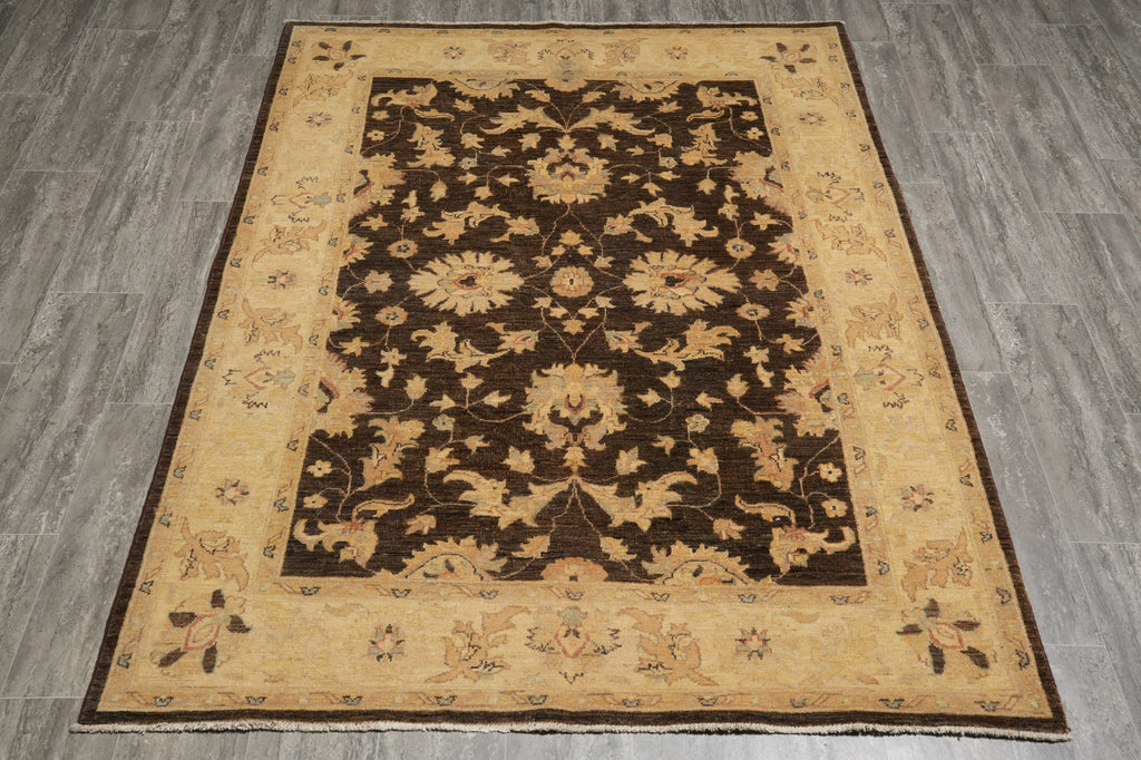 A rectangular area rug with a traditional floral pattern, featuring a dark brown center field and a warm beige border, laid out on a gray wood-look floor.