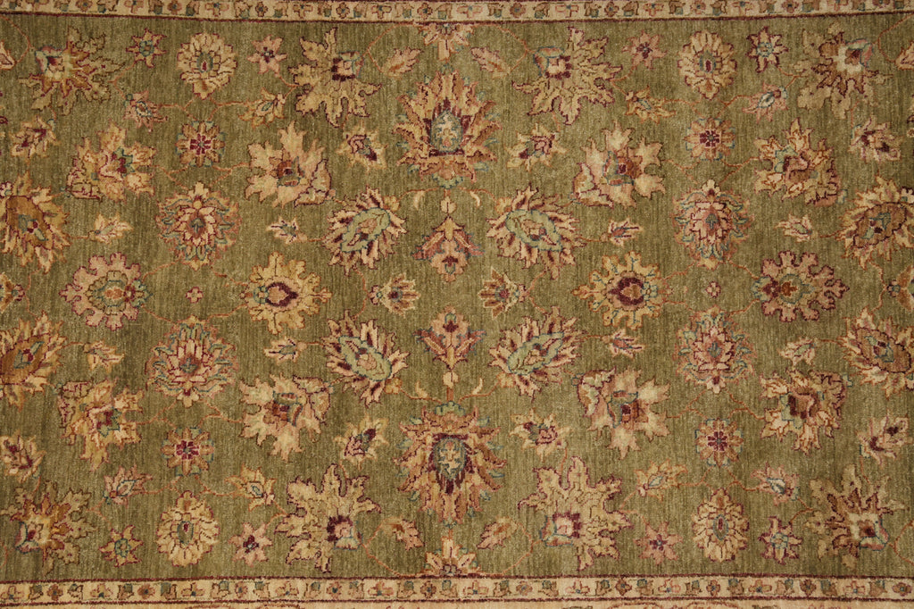 An antique-style area rug with an olive green field, featuring a repeating pattern of floral medallions in beige, rust red, and brown, finished with a detailed border.