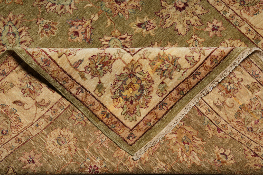 A folded vintage-style area rug with an intricate floral and medallion pattern in muted olive green, beige, and brown tones.