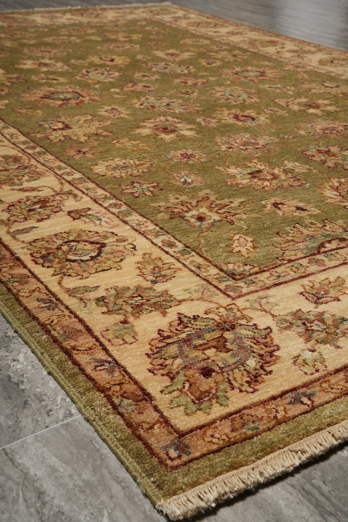 A traditional oriental area rug with an olive green field, beige border, and floral motifs, shown laid out on a gray stone floor.