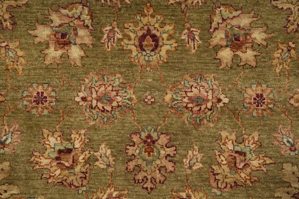 A close-up of a traditional patterned rug with an olive green background and ornate floral motifs in beige, rust red, and light blue.