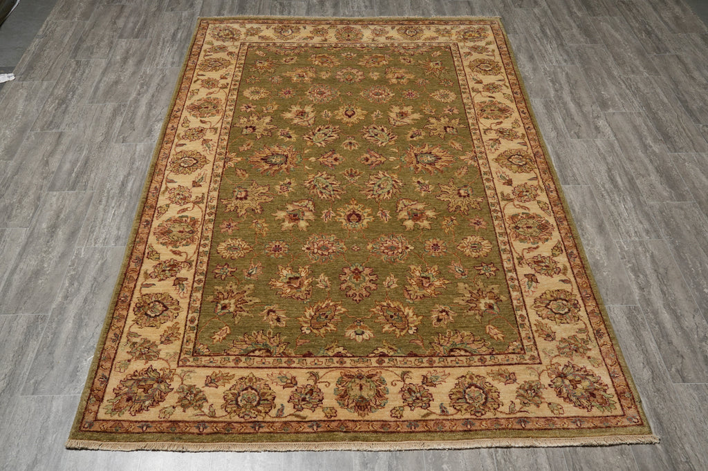 A rectangular area rug with an ornate floral medallion pattern, featuring a muted olive green center field and beige borders, laid out on a gray wood-look floor.