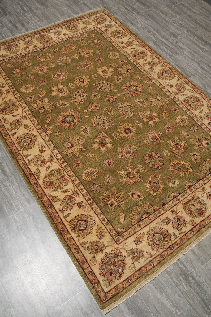 An oriental-style area rug with a sage green field, beige borders, and intricate floral motifs in muted red, brown, and blue, shown laid out on a gray wood-look floor.