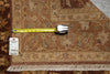 Load image into Gallery viewer, A close-up of a patterned area rug in warm brown and beige tones with fringe along one edge, shown with a yellow tape measure and a white inventory tag on top.
