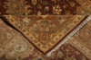 Load image into Gallery viewer, A close-up of a traditional patterned area rug, showing a folded corner that reveals the cream fringe and detailed floral motifs in shades of brown, beige, and muted green.