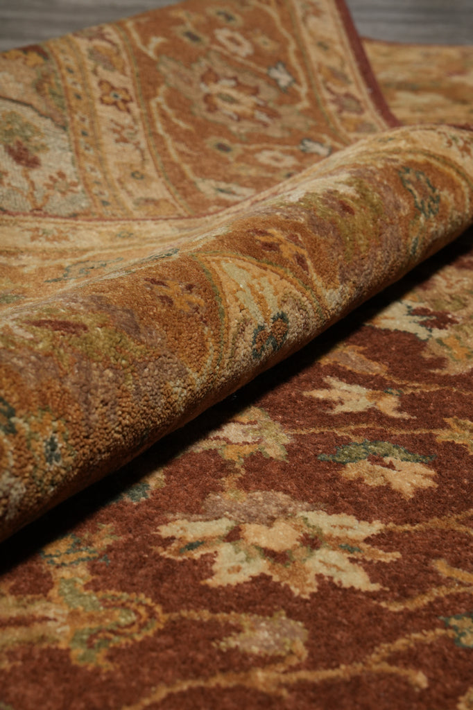 A close-up of a rolled area rug showing its detailed traditional pattern in warm brown, beige, and muted green tones.