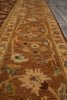 Load image into Gallery viewer, A close-up view of a traditional patterned area rug in warm brown, beige, and muted green tones, shown on a gray floor.