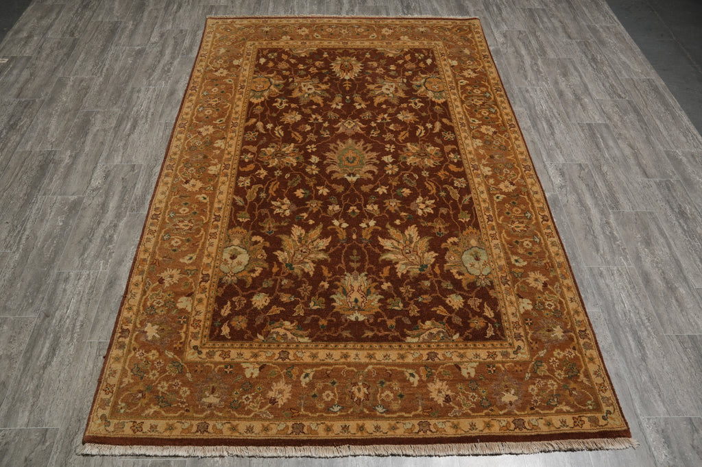 A traditional oriental area rug with a dark brown center and ornate floral patterns in beige, gold, and muted green, laid out on a gray wood-look floor.