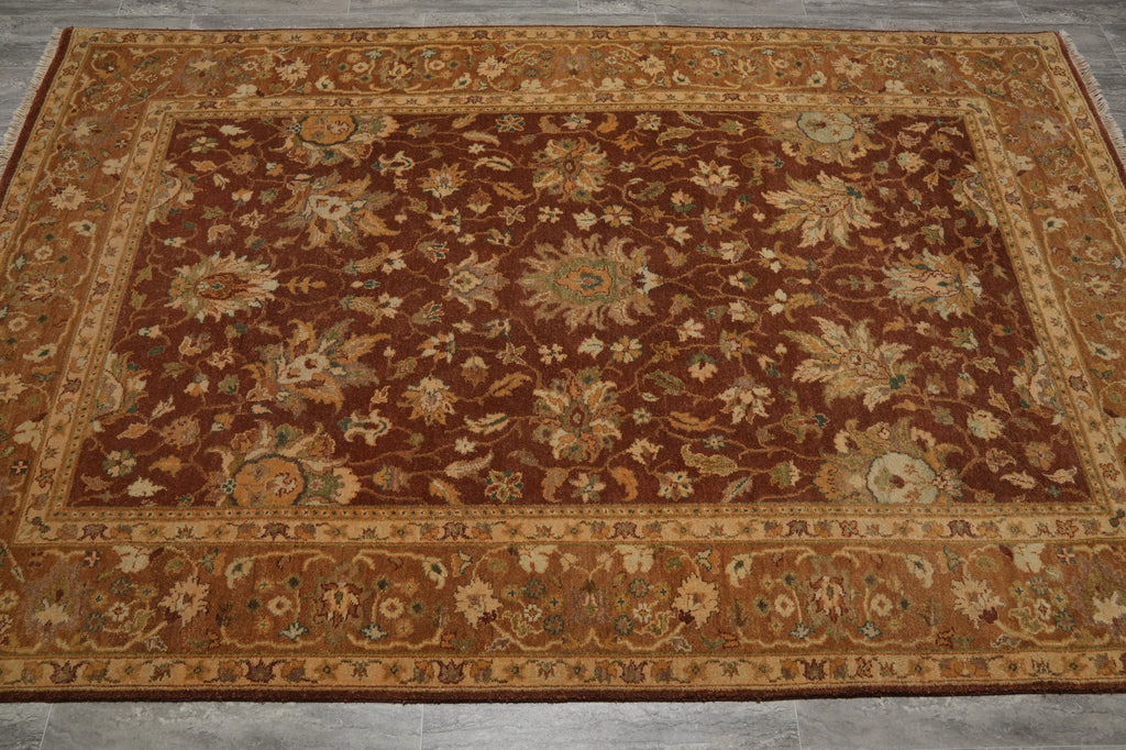 A rectangular traditional area rug with an intricate floral and medallion pattern, featuring a dark brown center field and a warm beige border, laid flat on a gray tiled floor.