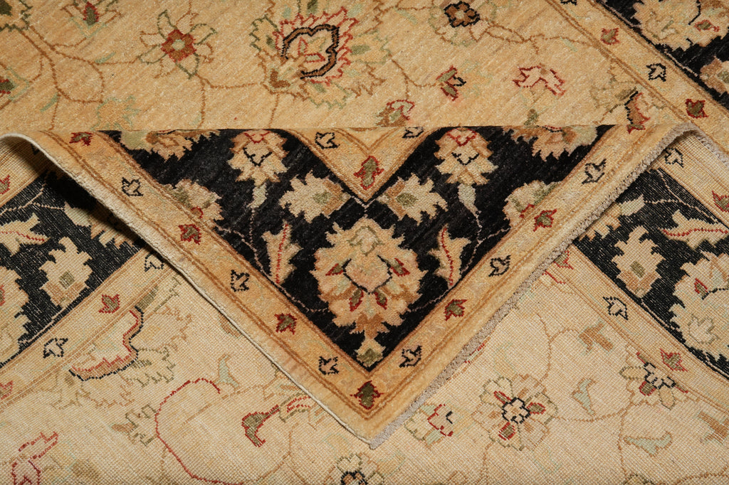 A close-up of a folded traditional patterned rug showing a cream and black floral design with beige and rust accents.