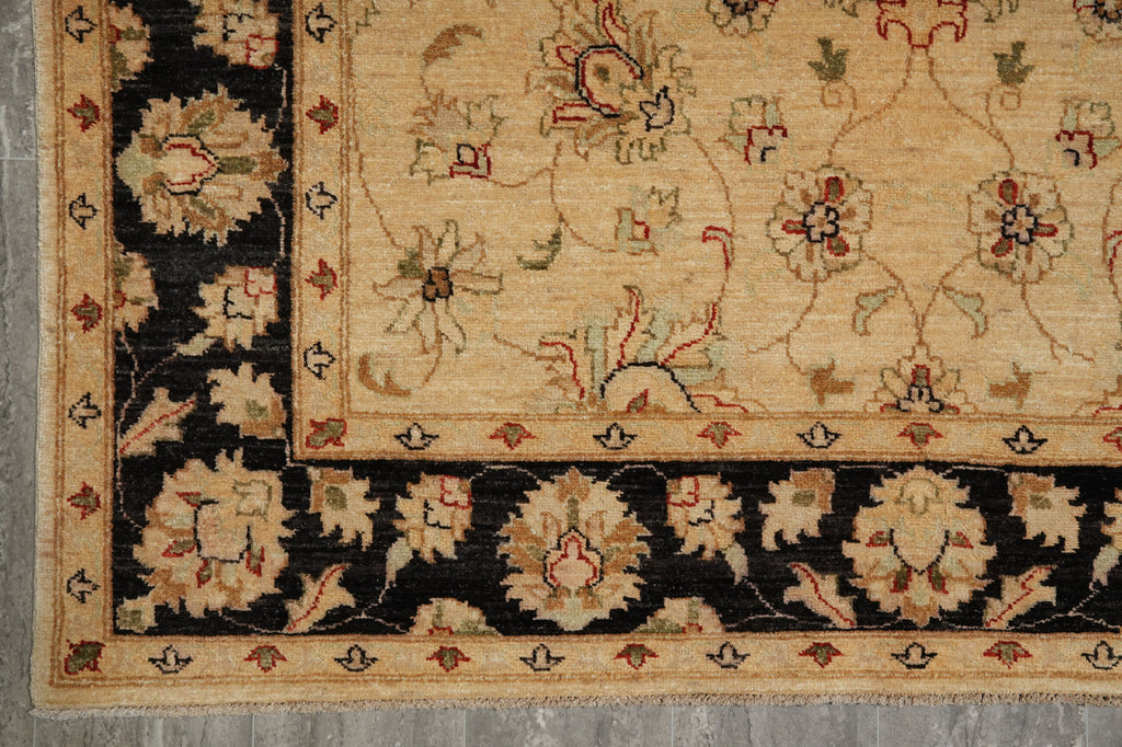 A close-up of an ornate area rug corner showing a beige field with floral motifs and a wide black border with cream and muted red detailing.