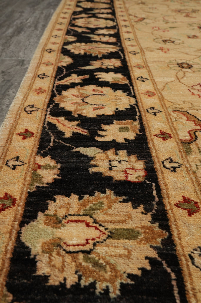 A close-up view of a traditional patterned area rug with a black center field, beige floral motifs, and cream borders, shown on a gray floor.