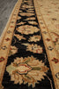 Load image into Gallery viewer, A close-up view of a traditional patterned area rug with a black center field, beige floral motifs, and cream borders, shown on a gray floor.