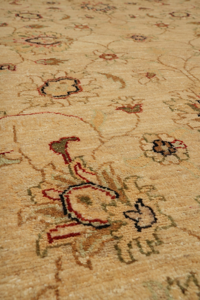 Close-up of a beige area rug with a traditional floral and vine pattern in muted red, green, and dark blue accents.