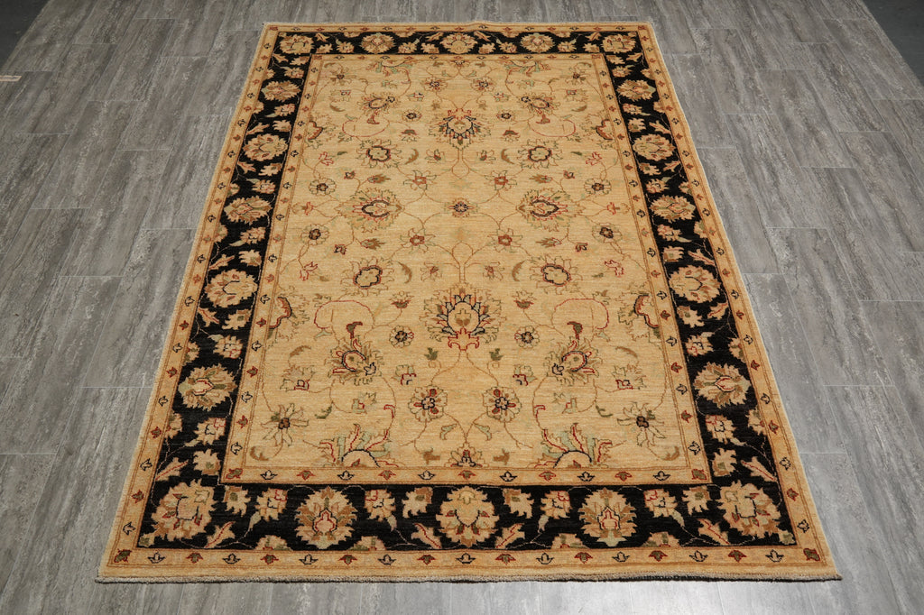 A rectangular area rug with a traditional floral pattern, featuring a beige center field, a black border, and a tan outer border, shown on a gray wood-look floor.