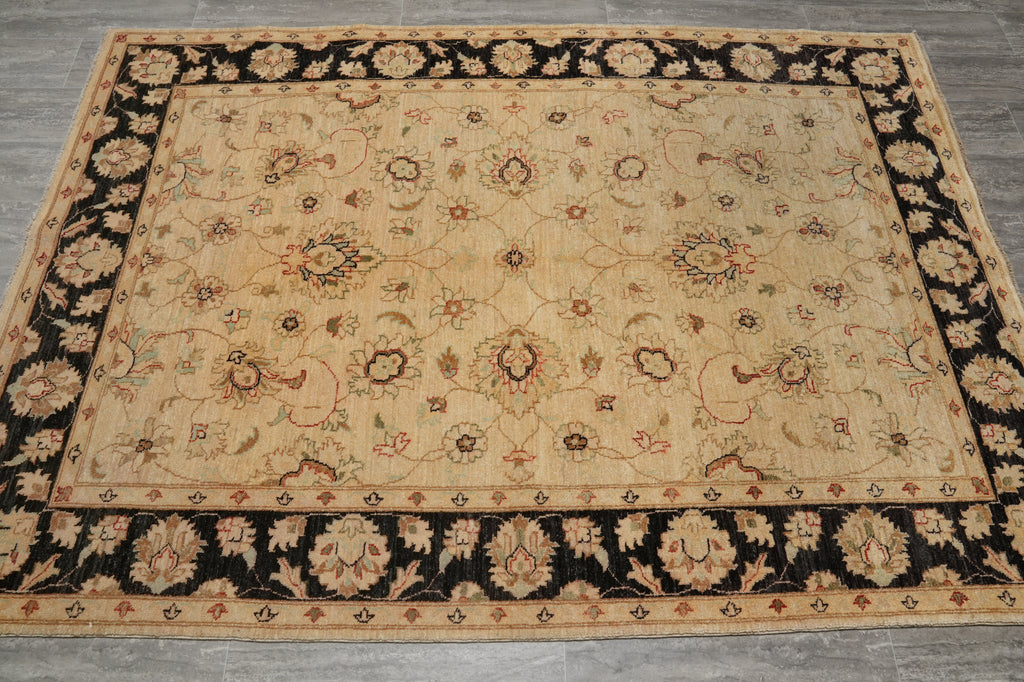 A rectangular vintage-style area rug with a beige center field and a wide black border, featuring intricate floral and medallion motifs in beige, brown, and muted red, laid out on a gray floor.