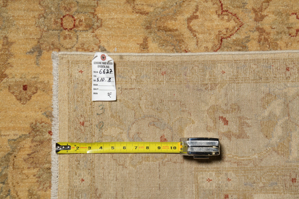 A folded beige patterned rug laid flat on a matching patterned surface, with a yellow tape measure placed along one edge and a small inventory tag attached near the top.