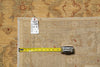 Load image into Gallery viewer, A folded beige patterned rug laid flat on a matching patterned surface, with a yellow tape measure placed along one edge and a small inventory tag attached near the top.