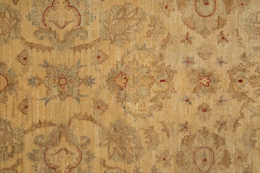 A close-up of a vintage-style area rug featuring a distressed, faded floral and scroll pattern in beige, tan, muted blue-gray, and rust red.