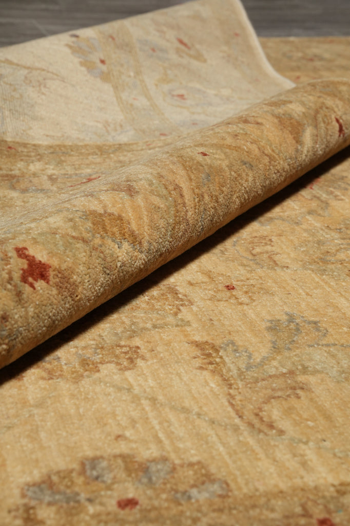 A close-up of a rolled area rug showing its textured, vintage-style pattern in warm beige, tan, and muted red accents.