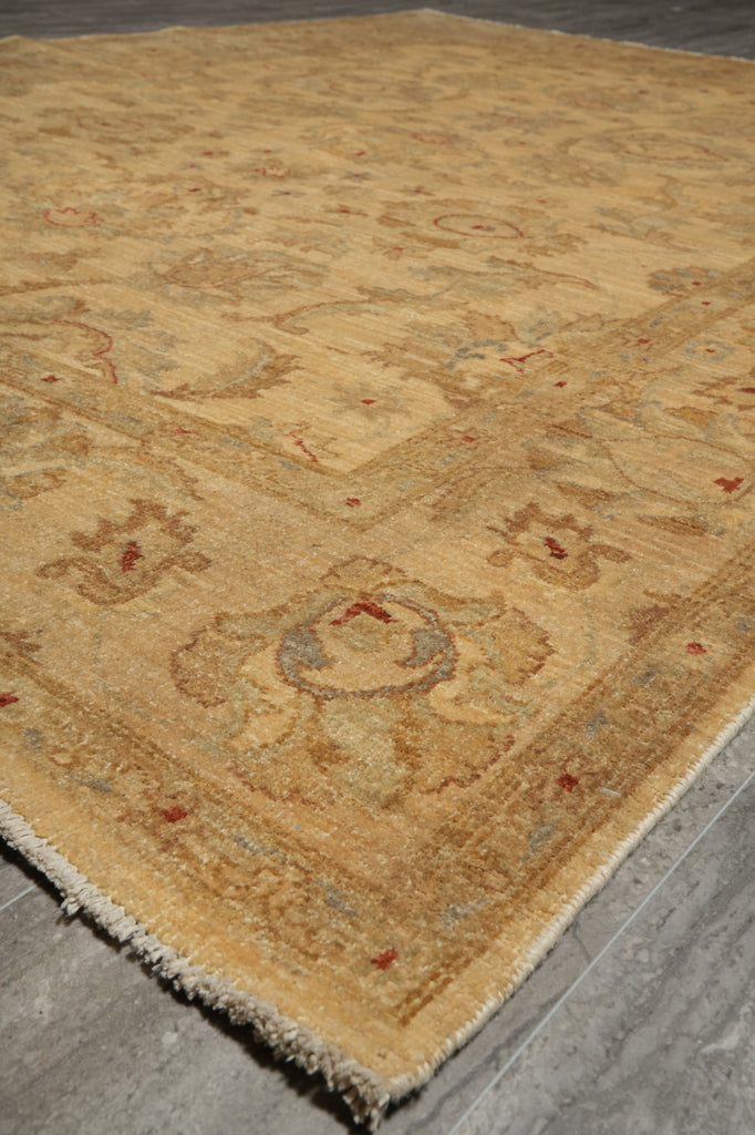 A close-up view of a traditional area rug with a warm beige and tan base, featuring faded floral motifs and small red accents, laid out on a gray wood floor.