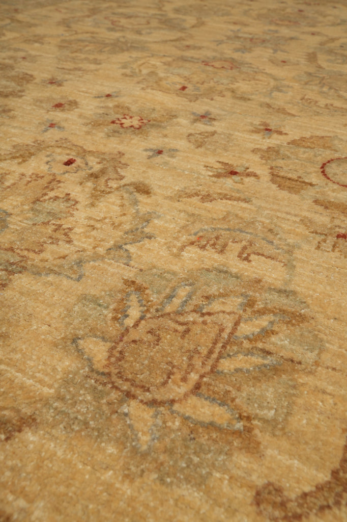 A close-up view of a traditional patterned rug in warm beige and tan tones with muted blue-gray and small red accents.