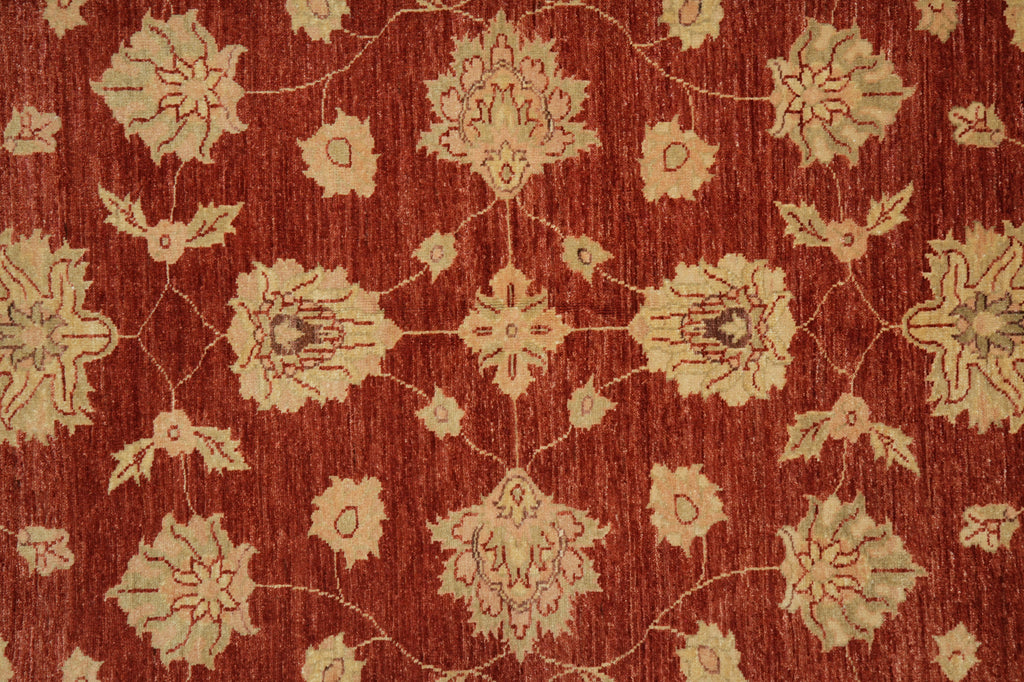 A close-up of a traditional patterned rug featuring a warm rust red background with beige floral motifs and delicate vine details.