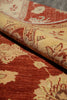 Load image into Gallery viewer, A close-up of a patterned area rug with a folded corner showing its texture and reverse side. The design features a warm rust red and beige floral motif.