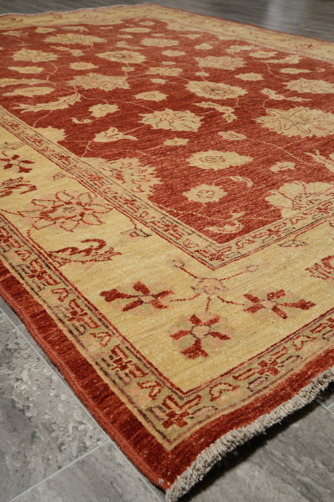 A traditional oriental-style area rug with a warm rust red and beige floral pattern, shown laid out on a gray tiled floor.