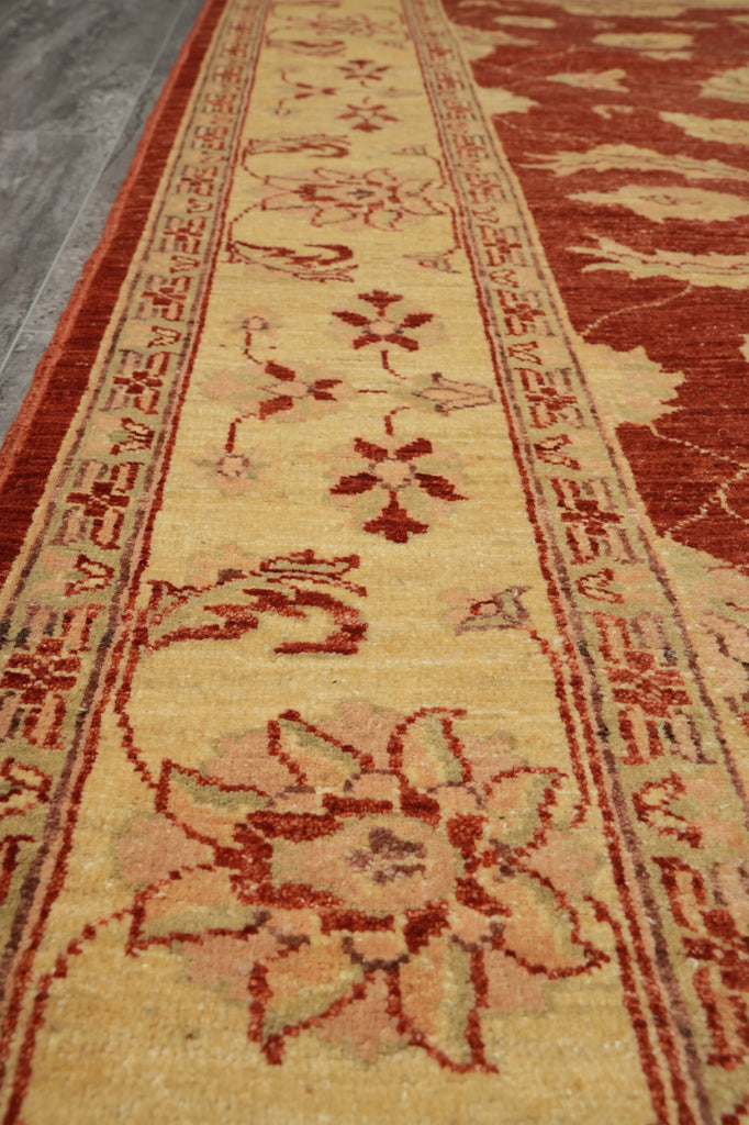 A close-up view of a traditional patterned area rug with a warm beige center, red and rust borders, and floral motifs.
