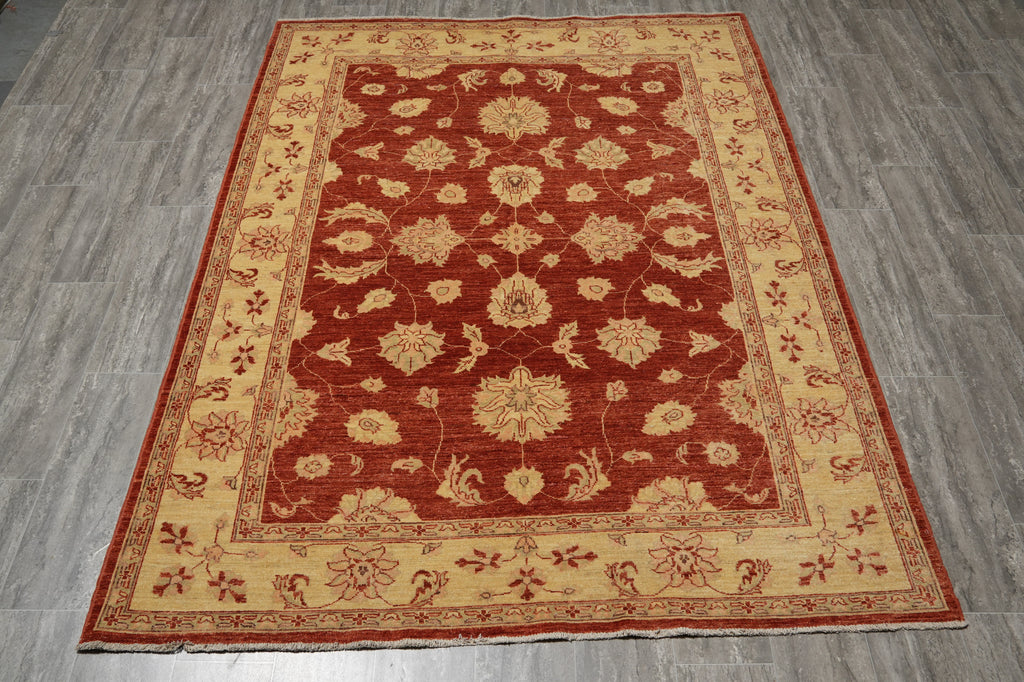 A rectangular area rug with a traditional floral pattern, featuring a deep red center field and a beige border, laid out on a gray wood-look floor.