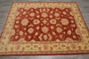 Load image into Gallery viewer, A rectangular area rug with a traditional floral pattern, featuring a deep red center field and a warm beige border, laid out on a gray wood floor.