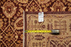 Load image into Gallery viewer, A close-up of a patterned area rug with a beige center and dark brown borders, shown with a yellow tape measure and a small product tag on top.