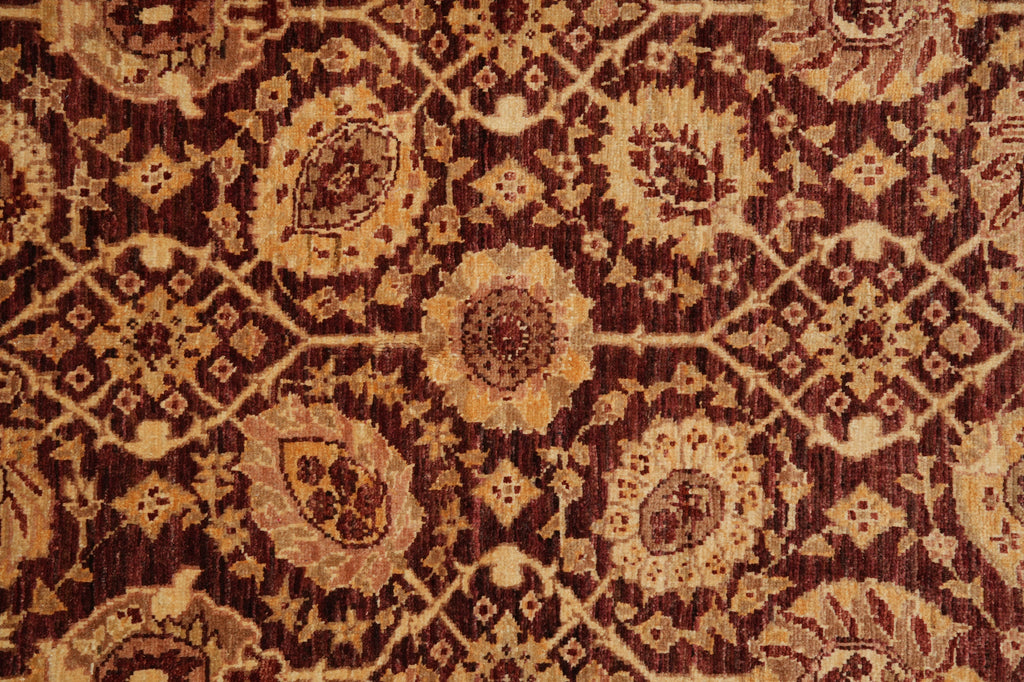 A close-up of a traditional patterned rug featuring a repeating floral and geometric design in dark brown, rust red, and beige.