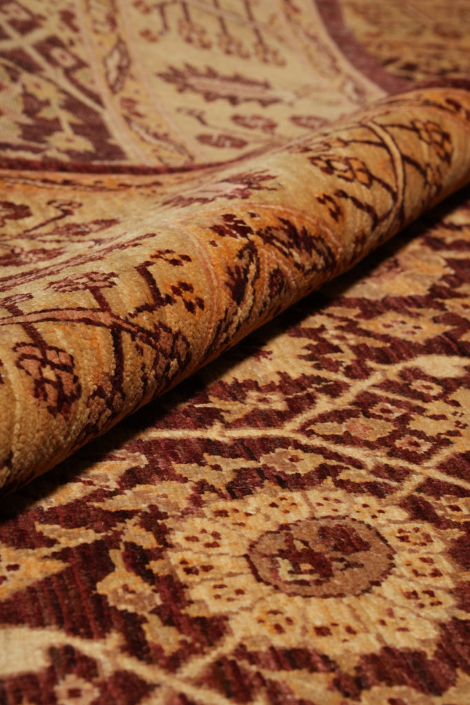 A close-up of a patterned area rug with one corner rolled back, showing its woven texture and traditional floral motifs in beige, brown, and burgundy tones.