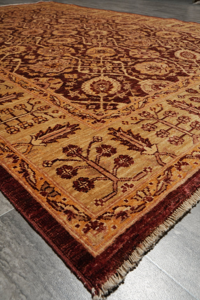 A traditional oriental-style area rug with an intricate floral and geometric pattern in warm tan, rust red, and dark brown, shown laid out on a gray tiled floor.