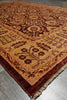 Load image into Gallery viewer, A traditional oriental-style area rug with an intricate floral and geometric pattern in warm tan, rust red, and dark brown, shown laid out on a gray tiled floor.