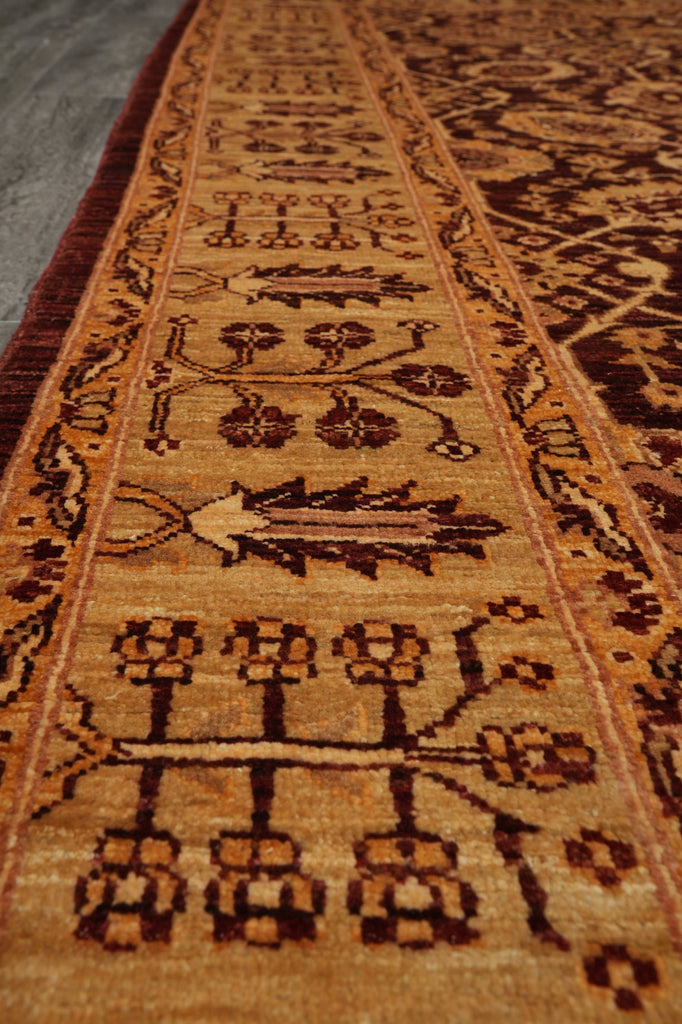 A close-up view of a traditional patterned area rug with a warm tan and brown base, featuring dark brown geometric and floral motifs.