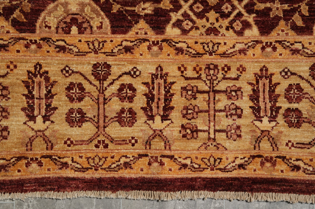 A close-up of a patterned rug showing a traditional design with floral motifs in dark red and brown on a warm beige background, with a fringed edge visible at the bottom.