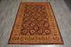 Load image into Gallery viewer, A rectangular traditional area rug with an intricate floral and geometric pattern in shades of brown, rust, and beige, laid out on a gray wood-look floor.