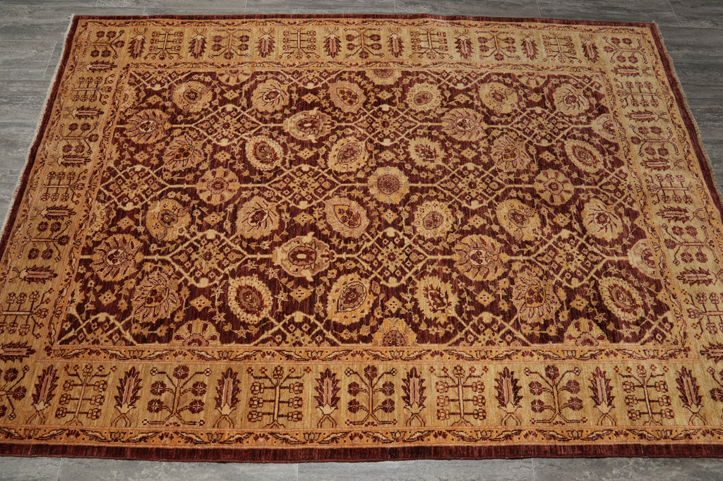 An oriental-style area rug with an intricate floral and geometric pattern in dark brown, rust red, and golden beige, laid out on a gray wood floor.