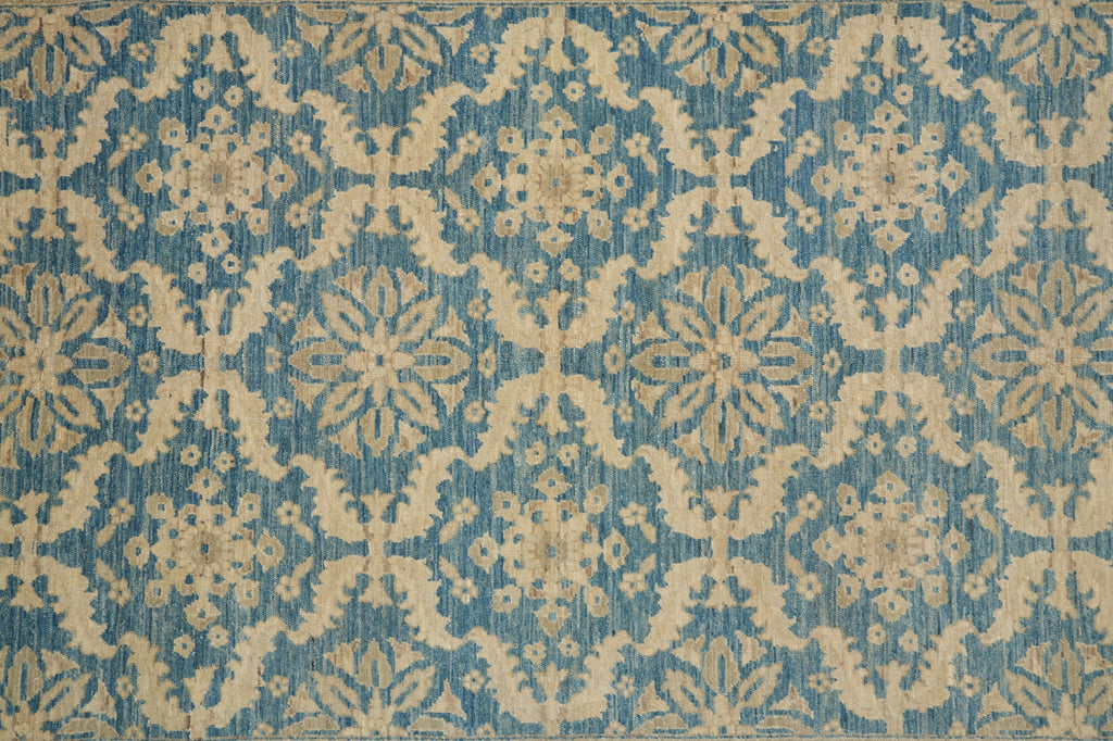 A close-up of a patterned textile or rug featuring a repeating damask-style floral motif in blue and warm beige.