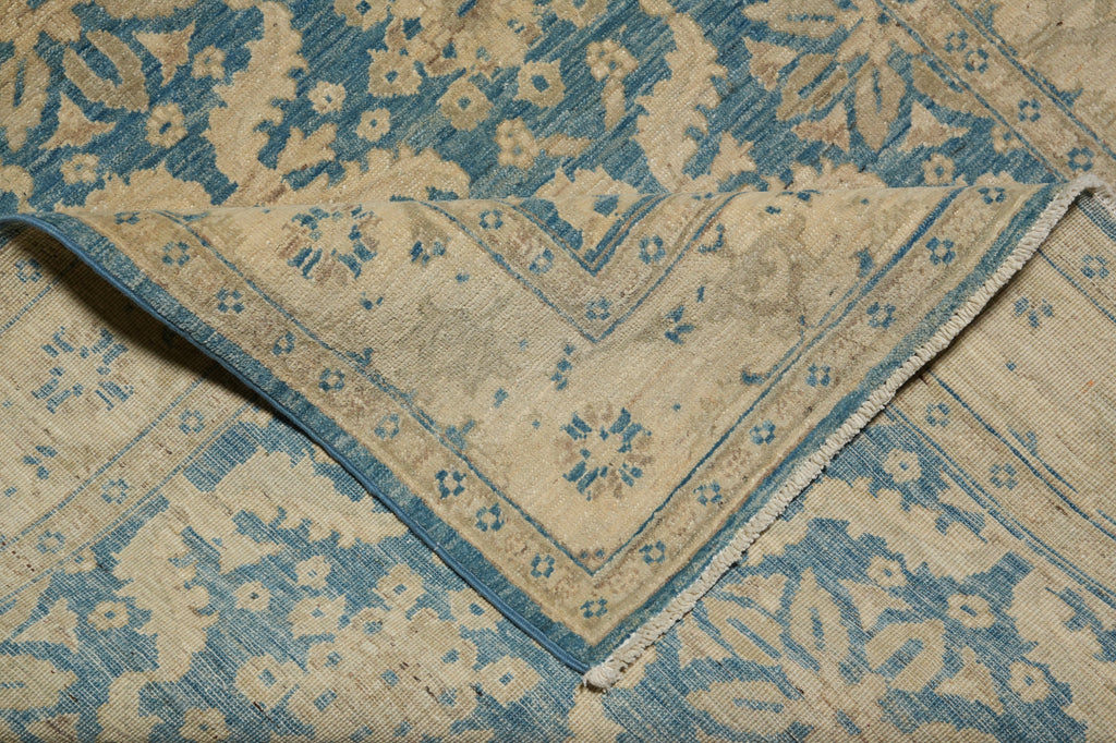 A close-up of a folded area rug showing its intricate traditional pattern in dusty blue and warm beige/cream tones.